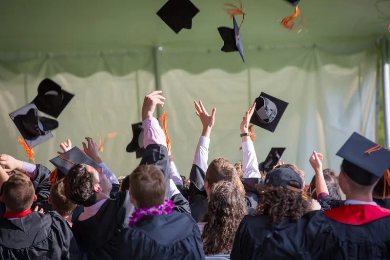 University graduates in gowns celebrating by throwing their caps into the air.
